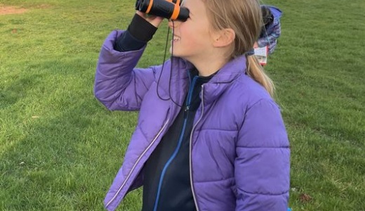 Y5 pupil bird watching on the school field.